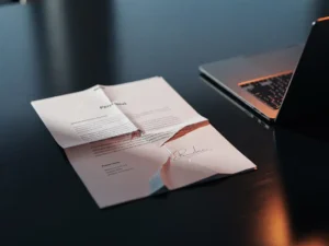Scheef liggend zakelijk voorstel op vergadertafel met open laptop, rode schaduwen over witte pagina's, kantooromgeving.